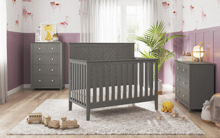 A modern nursery featuring the Child Craft Atwood 4-in-1 Convertible Crib in Lunar Gray, matching dressers, plush rug, toy train, stuffed animals, and potted plant. Sunlight streams through sheer curtains over animal-themed wallpaper.