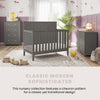 A modern nursery features the Child Craft Atwood 4-in-1 Convertible Crib in Lunar Gray, surrounded by a chevron dresser and chest on a light rug. Mauve and white walls with animal prints, plush toys, and plants create a cozy, sophisticated feel.