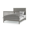 The Child Craft Atwood 4-in-1 Convertible Crib in Lunar Gray features vertical slats and a chevron-patterned headboard, shown with white and gray bedding and pillows.