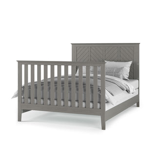 The Child Craft F06401 Full-Size Bed Rail in Lunar Gray features sturdy wooden rails, a slatted footboard, chevron-patterned headboard, and is compatible with a crib conversion kit; shown with white and gray bedding.