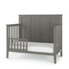 The Child Craft Atwood 4-in-1 Convertible Crib in Lunar Gray features a high chevron-patterned headboard, open side rails, and comes with a fitted white mattress.