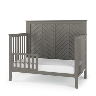 The Child Craft F09501 Toddler Guard Rail in Lunar Gray features strong wood construction, chevron-patterned design, side rails for safety, and pairs perfectly with a white mattress for a sturdy, modern look in any child’s bedroom.