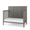 The Child Craft Atwood 4-in-1 Convertible Crib in Lunar Gray features a slatted headboard and sides, a chevron-patterned back panel, and includes a plain white mattress.