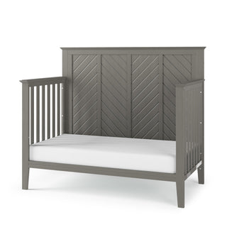 The Child Craft Atwood 4-in-1 Convertible Crib in Lunar Gray features a slatted headboard and sides, a chevron-patterned back panel, and includes a plain white mattress.