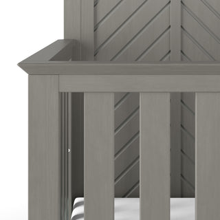 Close-up of the corner of the Child Craft Atwood 4-in-1 Convertible Crib in Lunar Gray, showing a white mattress, vertical slats, and a chevron pattern on the back panel.