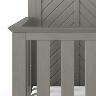 Close-up of the corner of the Child Craft Atwood 4-in-1 Convertible Crib in Lunar Gray, showing a white mattress, vertical slats, and a chevron pattern on the back panel.