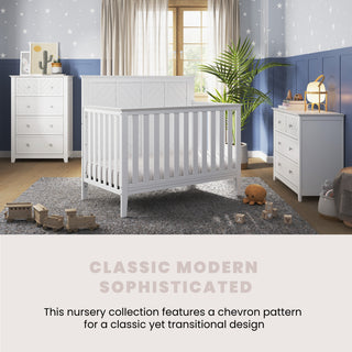 A modern nursery features the Child Craft Atwood 4-in-1 Convertible Crib in matte white, matching furniture, blue and gray star-patterned walls, soft toys, a cozy rug, and gentle lighting for a stylish, welcoming space.