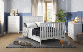 A cozy bedroom features the Child Craft Atwood 4-in-1 Convertible Crib in Matte White, matching dressers and nightstand, star-patterned wallpaper, a large window with light curtains, toys on a gray rug, and a green potted plant by the window.