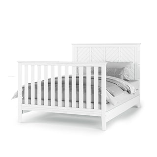 The Child Craft Atwood 4-in-1 Convertible Crib in Matte White features vertical slats on the headboard and footboard, dressed in gray and white bedding and pillows, shown against a plain white background.