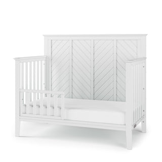 The Child Craft Toddler Guard Rail in Matte White features sturdy wood construction, a chevron-patterned headboard, partial side panels, and an open front, shown on a white background.