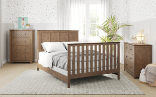 A bright bedroom features Child Craft's Atwood 3-Drawer Dresser in Cocoa Bean, a cozy bed, nightstand, and chest of drawers. Patterned wallpaper, a large window with sheer curtains, and a potted plant complete the inviting space.