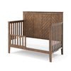 The Child Craft Toddler Guard Rail in Cocoa Bean features a tall, chevron-patterned headboard, vertical slats on both sides, a white mattress, and a natural brown finish. Shown against a plain white background.