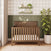 Cocoa Bean Child Craft Atwood 4-in-1 Convertible Crib with a chevron-patterned headboard, positioned against a green paneled wall with nursery decor on two shelves above and a large potted plant to the side.