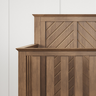 A close-up of the Child Craft Atwood 4-in-1 Convertible Crib in Cocoa Bean features a modern wooden design with geometric herringbone headboard and footboard, set against a white paneled wall.