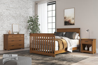 A modern bedroom features a wooden bed frame, Child Craft Redmond 3 Drawer Dresser in Coach Cherry, matching nightstand, neutral bedding, large window with white curtains, potted plant, floor lamp, wall art, and a gray rug.