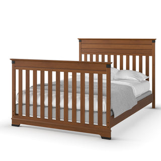 The Child Craft Redmond 4-in-1 Convertible Crib in Coach Cherry features vertical slats on the headboard and footboard, shown with neatly arranged white pillows, white sheets, and a gray blanket.
