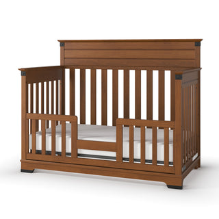 The Child Craft Redmond 4-in-1 Convertible Crib in Coach Cherry features a high back panel, slatted sides, an open front with a low safety rail, and includes a white mattress. Shown on a white background.