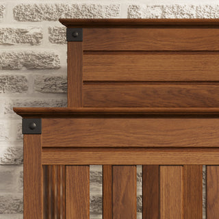 Close-up of the Child Craft Redmond 4-in-1 Convertible Crib headboard in Coach Cherry, highlighting vertical wooden slats, black metal accents, and a warm brown finish that showcases the natural wood grain against a light gray brick wall.