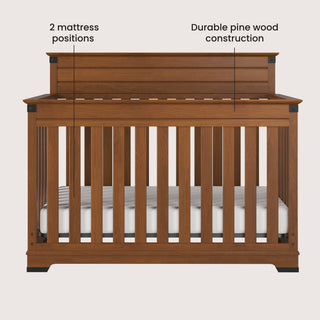 Front view of the Child Craft Redmond 4-in-1 Convertible Crib in Coach Cherry, featuring slatted sides and back, two labeled mattress positions, and sturdy pine wood construction. Shown with a white mattress inside.