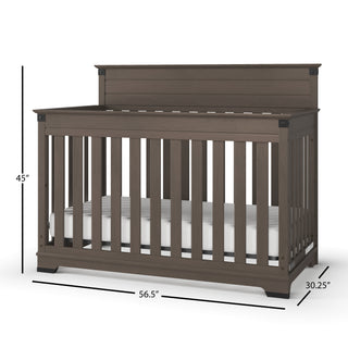 The Child Craft Redmond 4-in-1 Convertible Crib in Dapper Gray features vertical slats, a solid headboard, and includes a white mattress. Dimensions: 45" H x 56.5" W x 30.25" D. Shown on a white background.