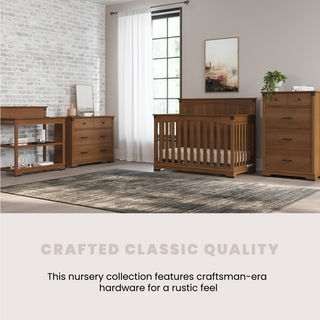 A nursery with wooden furniture and a large window features the Child Craft Redmond 3 Drawer Dresser in Coach Cherry. Set against a white brick wall, the dresser boasts craftsman-era hardware for a classic, rustic touch.
