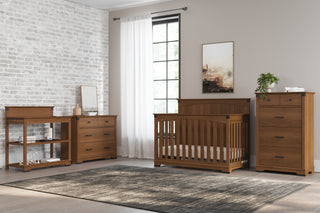 A modern nursery with the Child Craft Redmond Full Panel 4-in-1 Convertible Crib in Coach Cherry, matching dresser, changing table, and tall chest. The space features light walls, a large window with white curtains, a rug, and minimal decor.