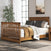 A Child Craft F06424 Full-Size Bed with Coach Cherry rails is featured in a bright bedroom, dressed in brown and white bedding, near a large window, gray rug, green plant, and a nightstand.