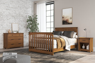 A modern bedroom with wooden furniture, featuring the Child Craft Redmond Full Panel 4-in-1 Convertible Crib in Coach Cherry, a bed, nightstand, dresser, neutral decor, a patterned rug, plant, large window with white curtains, and a wall painting.