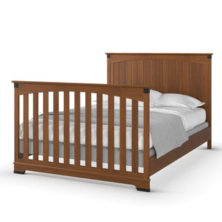 The Child Craft F06424 features full-size bed rails in a warm Coach Cherry finish, with a wooden frame and vertical slats on the headboard and footboard, shown with white pillows and a gray blanket.