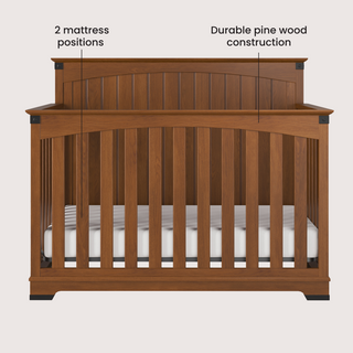 Front view of the Child Craft Redmond Full Panel 4-in-1 Convertible Crib in Coach Cherry, shown with a white mattress. Labels highlight “2 mattress positions” and “Durable pine wood construction.” Ideal for any baby nursery.