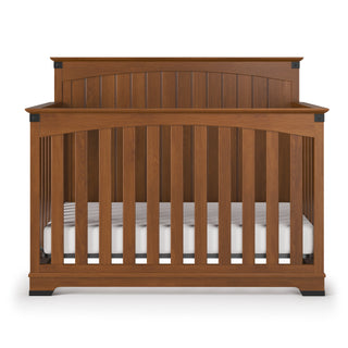 The Child Craft Redmond Full Panel 4-in-1 Convertible Crib in Coach Cherry features vertical slats, a high solid headboard, and includes a white mattress—adding style and versatility to any nursery.