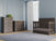A modern nursery features light blue paneled walls, a large window with white curtains, a gray crib, Child Craft’s Redmond 3 Drawer Dresser in Dapper Gray with a small plant on top, a matching chest, a gray rug, and wood floors.