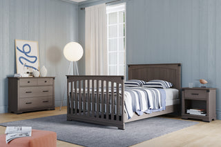 A modern bedroom features gray wood furniture—including a Child Craft Redmond Nightstand in Dapper Gray—plus a bed with striped bedding, dresser, round floor lamp, abstract art, and a large window with light curtains for natural light.