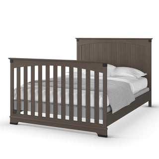 The Child Craft Redmond Full Panel 4-in-1 Convertible Crib in Dapper Gray features a slatted headboard and footboard, and is made up with white sheets, a gray blanket, and pillows.