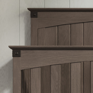 Close-up of two stacked Redmond Full Panel 4-in-1 Convertible Cribs by Child Craft in Dapper Gray, featuring vertical slats and decorative corner accents, set against a light-colored paneled wall.
