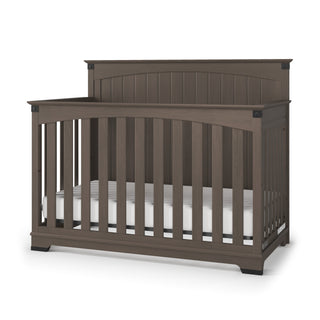 The Child Craft Redmond Full Panel 4-in-1 Convertible Crib in Dapper Gray features vertical side slats, a high solid headboard, and a white mattress. Its simple, modern design makes it a stylish and versatile nursery choice.