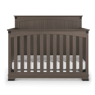 The Child Craft Redmond Full Panel 4-in-1 Convertible Crib in Dapper Gray features vertical slats, a curved headboard, and a white mattress, displayed against a white background.