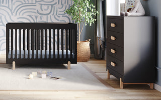 A modern mid-century nursery features the Child Craft Park Heights 4-In-1 Euro Crib in Caviar Black, a matching dresser, a potted plant, and toys on a beige rug. Sunlight streams through pale blue curtains onto patterned walls.