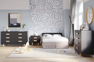 A modern nursery features the Child Craft Park Heights 4-In-1 Euro Crib in caviar black, two dark artisan dressers, abstract wall art, a round mirror, rocking horse, toys on a light rug, bold blue-and-white accent wall, and large sunlit windows.
