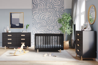 Modern nursery featuring the Child Craft Park Heights 4-In-1 Euro Crib in Caviar Black, matching dressers, a rocking horse, potted plant, abstract wall art, a round mirror, patterned wallpaper, and soft natural light for a stylish, heirloom-inspired space.