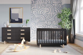 A modern mid-century nursery featuring the Child Craft Park Heights 4-In-1 Euro Crib in Caviar Black, a matching dresser, abstract wall art, potted plant, rocking horse, toys on a light rug, and blue and white curved wall patterns.