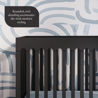 The Park Heights 4-In-1 Euro Crib in Caviar Black by Child Craft, crafted from Brazilian hardwood with rounded oval details, stands out for its sleek, modern style and heirloom-quality appeal against a white wall with blue accents.
