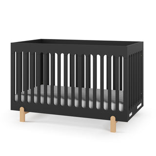 The Park Heights 4-In-1 Euro Crib by Child Craft features a sleek caviar black finish, vertical slats, light wooden legs, and a white mattress. Crafted from Brazilian hardwood, it adds minimalist, mid-century style and heirloom quality to any nursery.