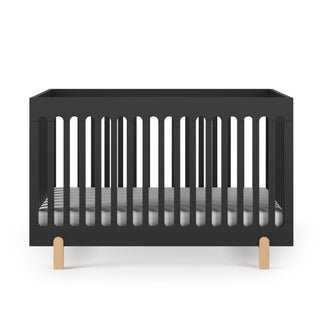The Child Craft Park Heights 4-In-1 Euro Crib in Caviar Black features vertical slats, light wooden legs, and a striped mattress. Its modern, minimalist style is ideal for a mid-century nursery, shown here against a white background.