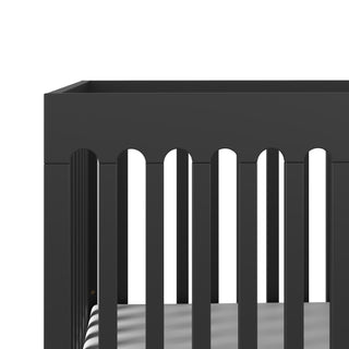 A close-up of the Park Heights 4-In-1 Euro Crib by Child Craft in Caviar Black, featuring vertical slats and an arched rail, ideal for a mid-century nursery, shown against a white background.