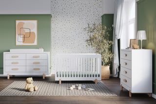 Modern nursery with green and white walls, a white crib and dresser, gray rug, teddy bear, potted plant, large window with sheer curtains, and a Child Craft Park Heights 4-Drawer Chest in Matte White featuring Brazilian hardwood accents.