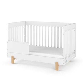 A Child Craft F09505 Toddler Guard Rail in matte white is shown on a plain white background, attached to a white crib with slatted sides and light wooden legs.