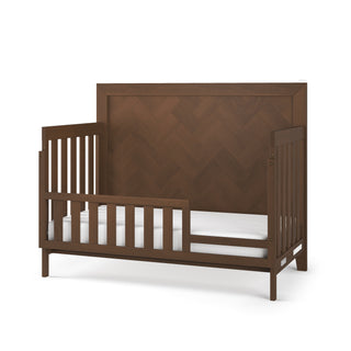 The Child Craft F09554 Toddler Guard Rail in Toasted Chestnut features a rich, dark brown finish and slatted design. Shown without bedding or mattress, it’s styled to match Child Craft cribs for lasting use after toddler bed conversion.