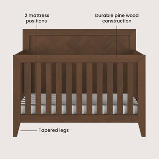 Front view of the Child Craft Kieran 4-in-1 Convertible Crib in Toasted Chestnut with slatted sides, labels highlighting its two mattress positions, durable pine wood build, and tapered legs.