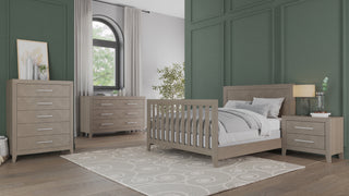 Modern bedroom with green paneled walls, a beige bed with white bedding, matching dresser and chest, the Child Craft Kieran Nightstand in Crescent Gray with silver handles, a round-patterned rug, and a large arched window with light curtains.